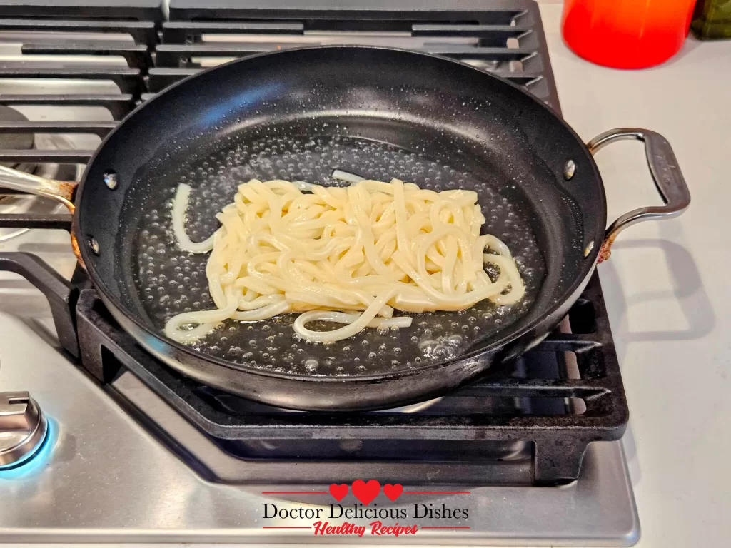 Udon noodles softening and separating in a hot pan while preparing Japanese Yaki Udon Recipe.