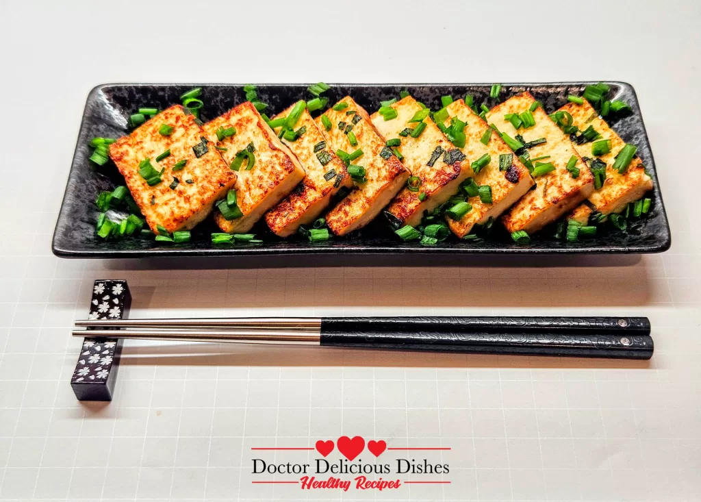 Golden tofu with oyster sauce arranged on a black plate with chopsticks.