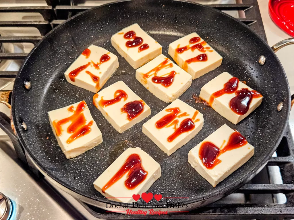 Oyster sauce being drizzled over tofu slices in a hot pan for Tofu with Oyster Sauce.