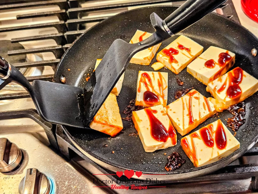 Using two spatulas to flip tofu without breaking it during Tofu with Oyster Sauce cooking.