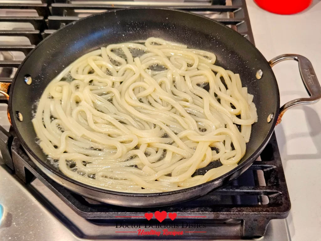 Fully softened udon noodles in a skillet ready for stir-frying pork and vegetables for Easy Yaki Udon Recipe.
