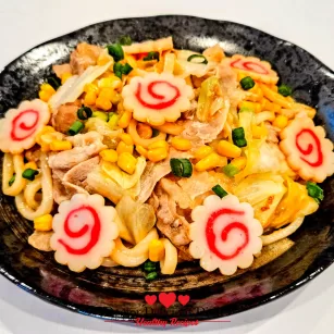 Easy Yaki Udon Recipe served in a black bowl with pork, cabbage, corn, and narutomaki fish cakes.