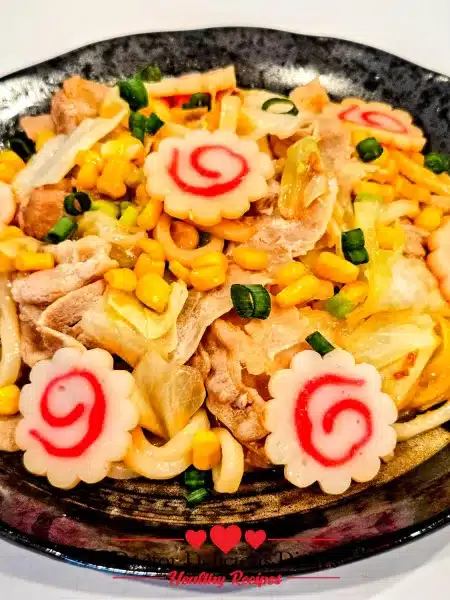 Easy Yaki Udon Recipe served in a black bowl with pork, cabbage, corn, and narutomaki fish cakes.