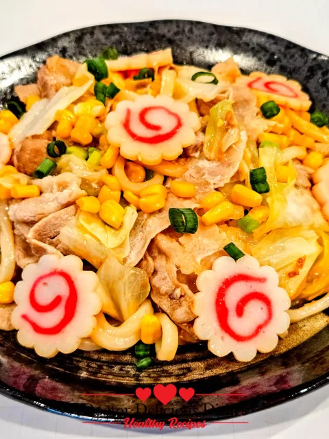 Easy Yaki Udon Recipe served in a black bowl with pork, cabbage, corn, and narutomaki fish cakes.