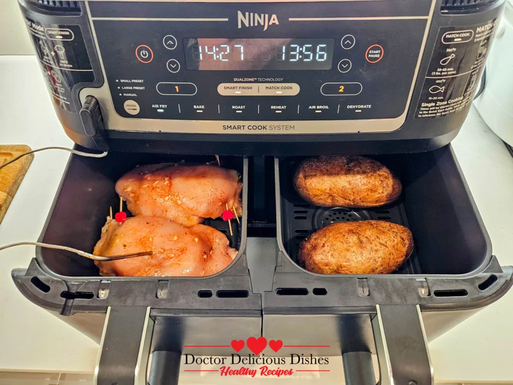 Air fryer baked potatoes cooking in the Ninja dual basket next to stuffed chicken breasts