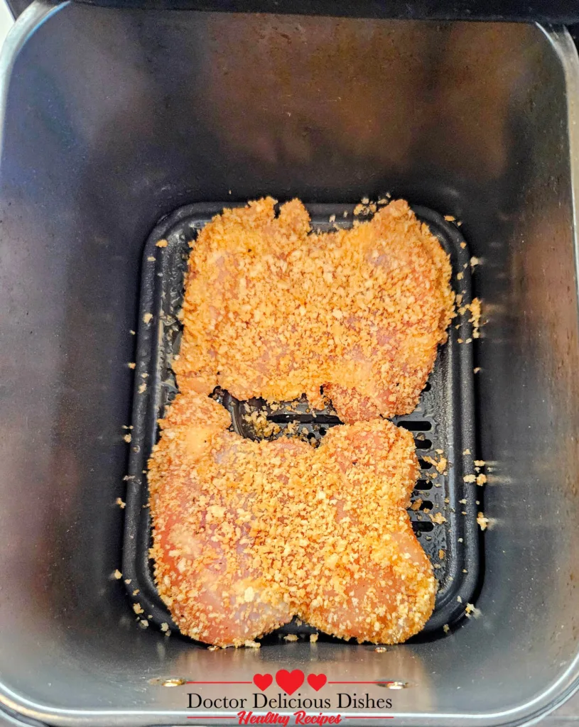 Breaded chicken thighs placed in the air fryer basket before cooking air fryer chicken katsu.