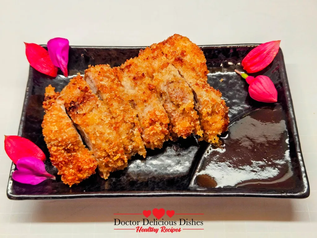 Air fryer chicken katsu sliced and arranged on a black plate with bright edible flowers and dipping sauce.