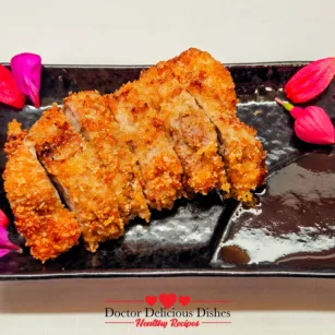 Air fryer chicken katsu recipe sliced and arranged on a black plate with bright edible flowers and dipping sauce.