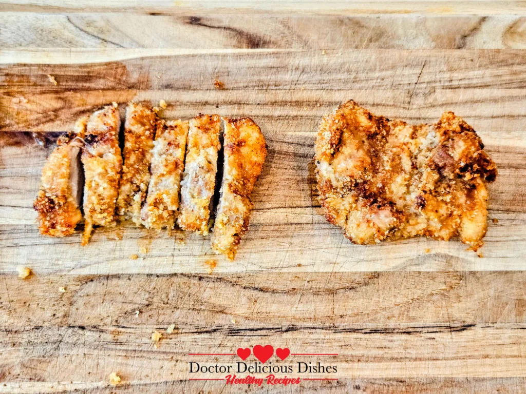 Crispy air fryer chicken katsu sliced on a wooden board next to an unsliced thigh for comparison.