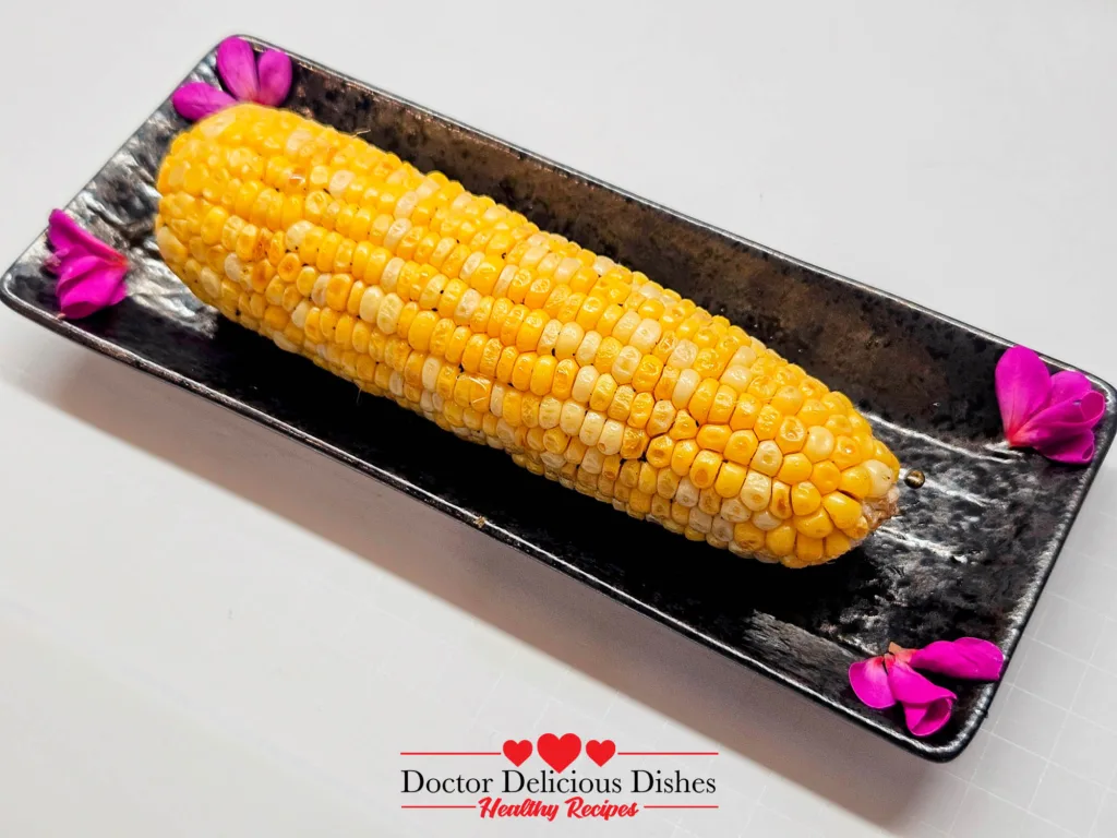 Air Fryer Corn on the Cob Yaki-Tōmorokoshi plated on a black dish with pink petals for garnish