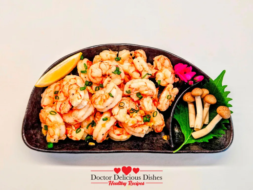 Garlic Butter Shrimp plated with lemon and green onions on a black dish.