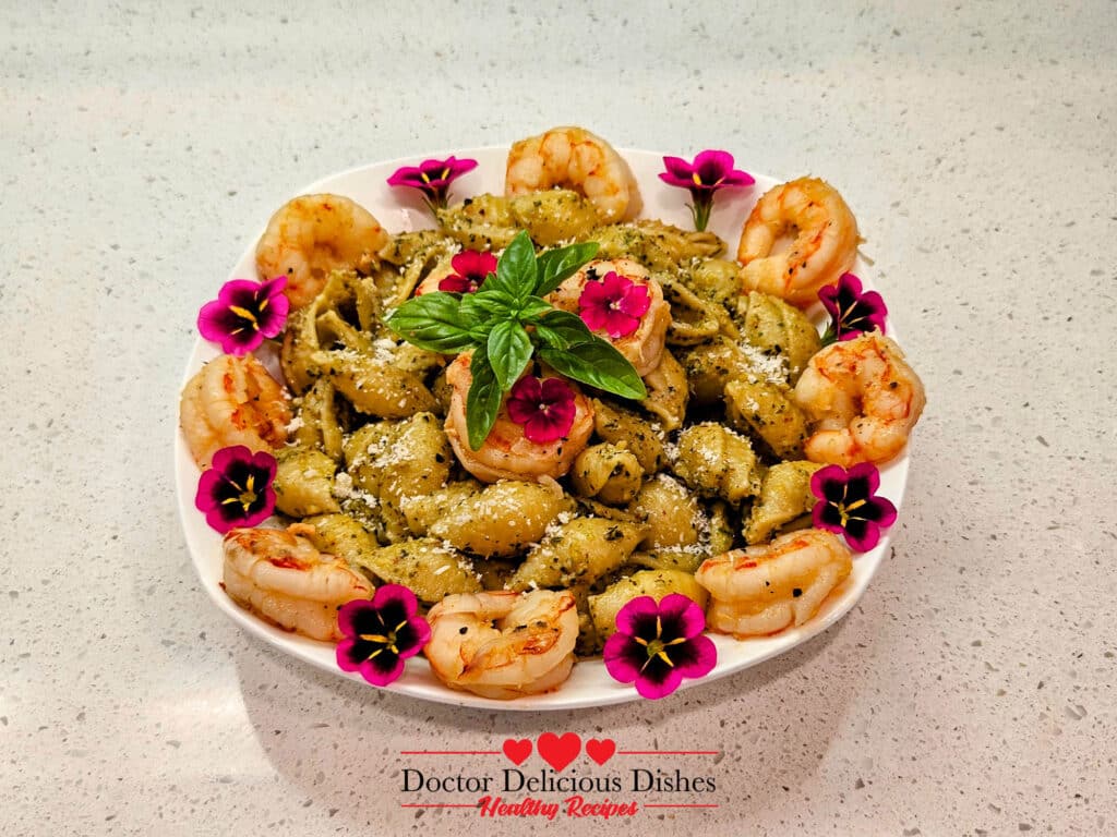Almond Pesto Shrimp Pasta with large shells, shrimp, Parmesan, fresh basil, and edible flowers on a white plate.