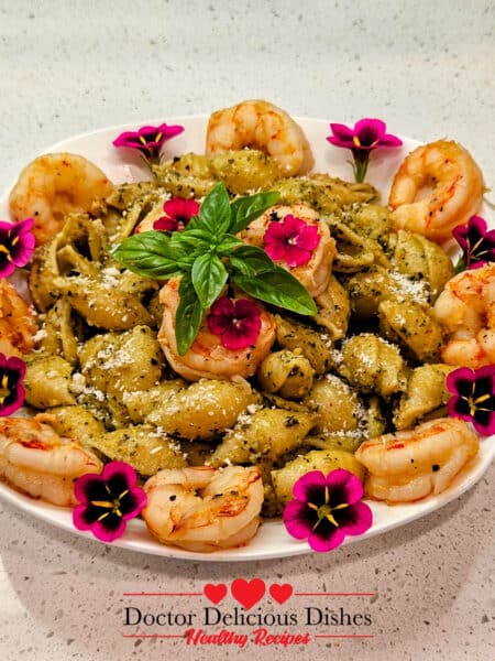 Almond Pesto Shrimp Pasta with large shells, shrimp, Parmesan, fresh basil, and edible flowers on a white plate.