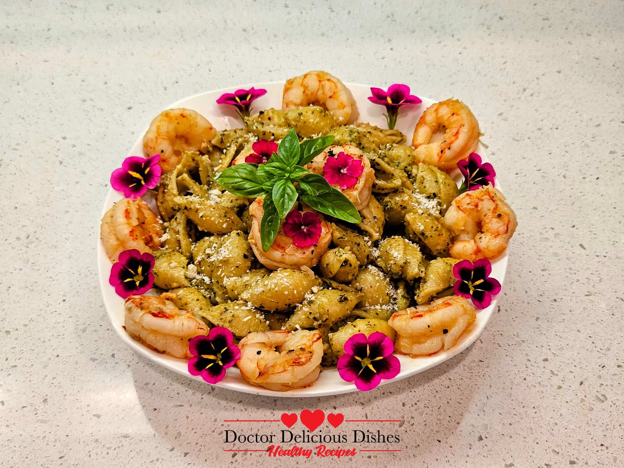 Almond Pesto Shrimp Pasta with large shells, shrimp, Parmesan, fresh basil, and edible flowers on a white plate.