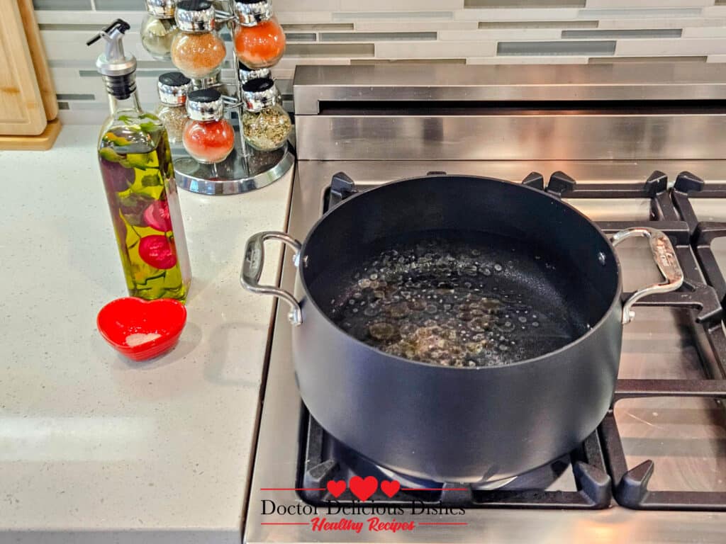 A large pot of salted water with olive oil boiling on the stove for cooking large shell pasta.