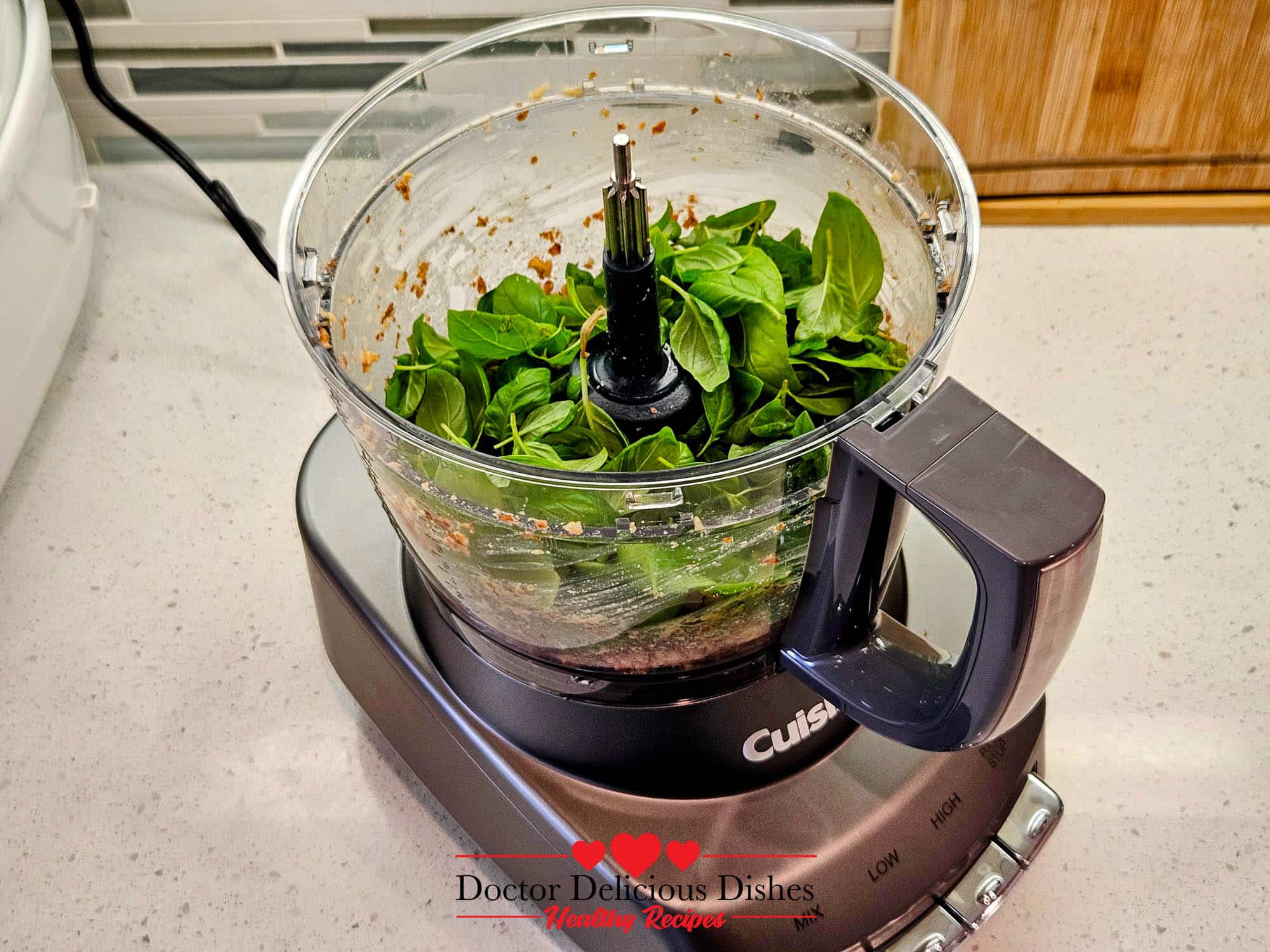 Fresh basil leaves added to a food processor with almonds and garlic for homemade almond pesto.