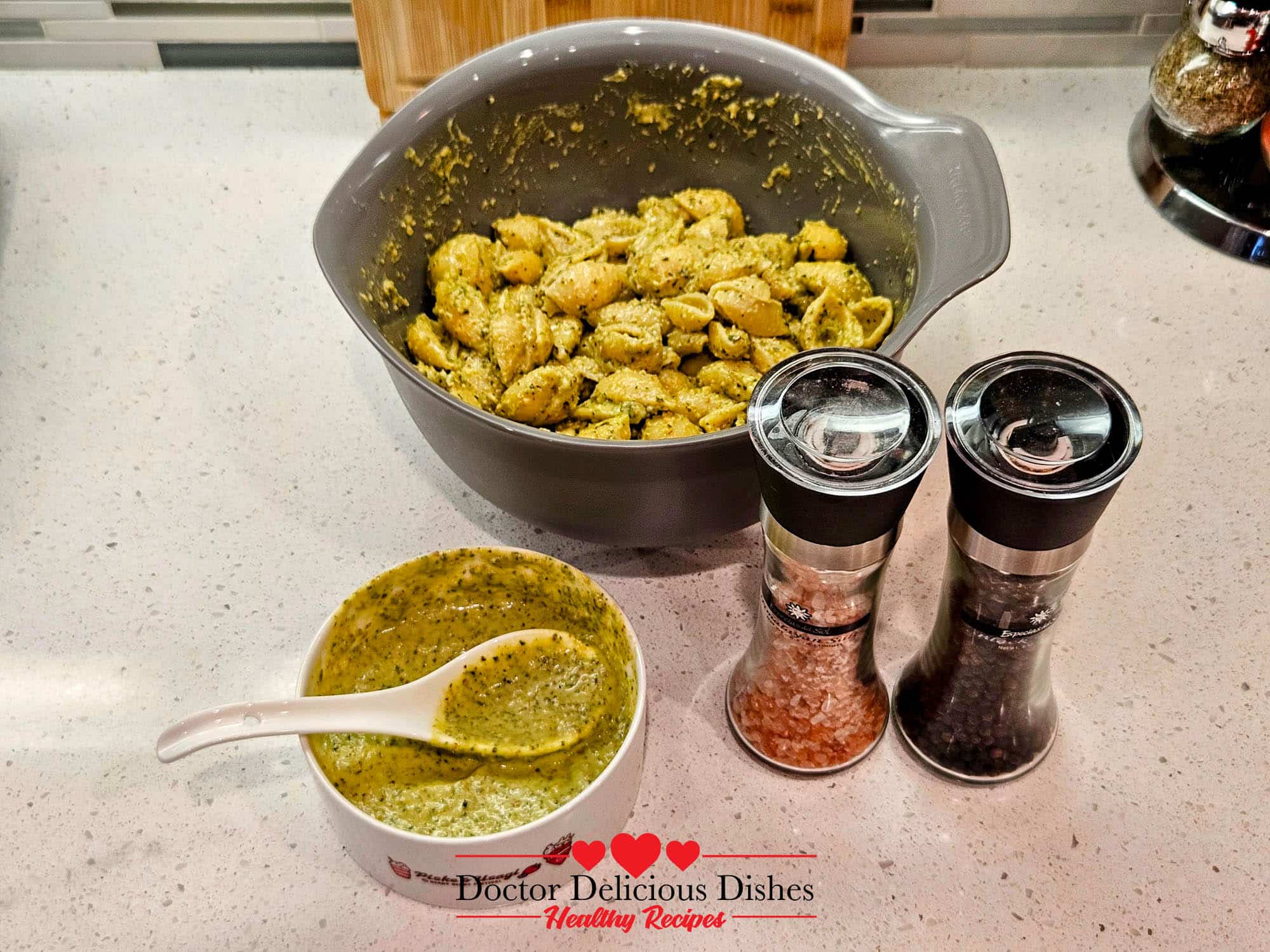 Large shell pasta mixed with homemade almond pesto, with extra pesto, salt, and pepper nearby.