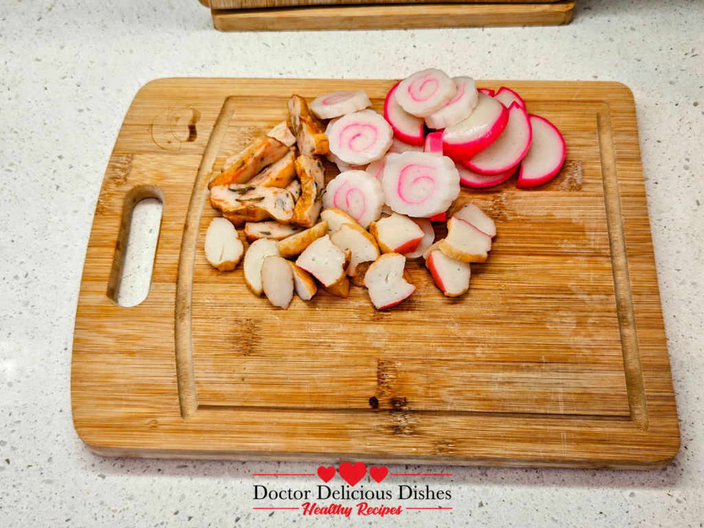 Sliced pink and white fish cakes on a cutting board for cold soba noodles